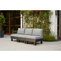 Moduláris, háromszemélyes kerti kanapé, szürke, tömör párnázattal, fekete lábakkal. Kellemes, zöld növényekkel körülvéve a teraszon található, tökéletes kültéri használatra.