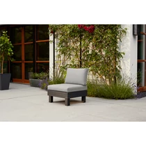 Mutatja az ELEMENTS 1 személyes kerti kanapét, szürke párnákkal, fekete fa kerettel, egy tágas teraszon elhelyezve. A kanapé körül virágok és növények találhatók, kellemes, természetes környezetben.