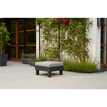 Moduláris ELEMENTS asztal párnával, szürke textilbőr ülőpárnával, fekete alumínium vázzal. Kertben elhelyezve, zöld növények és virágok között, időjárásálló és UV-védett kialakítással.