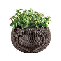 Kerek, sötétbarna műanyagos virágtartó, horgolt mintákkal díszítve, színes virágokkal betöltve. A kaspó kültéri és beltéri használatra egyaránt alkalmas, időjárásálló és könnyen tisztítható.