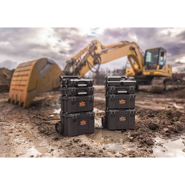 Két egymásra helyezett KETER Pro Gear 2.0 XL szerszámosláda látható, fekete színben, víz- és porszigetelésű kivitelben. A háttérben egy építkezési gép látható, sáros területen. A ládák tartós reteszekkel és puha markolattal