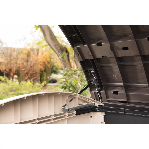 A kép egy STORE IT OUT ULTRA műanyag kerti tárolót mutat, amelynek nyitható lidje és kétszárnyú ajtaja könnyű hozzáférést biztosít. A háttérben kerti növények és fák láthatók.