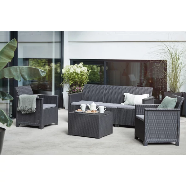 Háromszemélyes műrattan kerti kanapé és két fotel, szürke párnákkal, modern teraszon fotózva, mellette kisasztal, fehér teáskannával és poharakkal, valamint zöld növények háttérben.